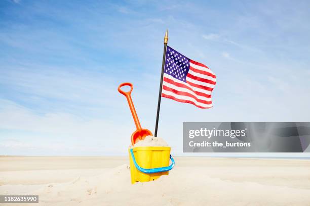 sand pail and shovel with usa flag on beach against blue sky - beach shovel stockfoto's en -beelden