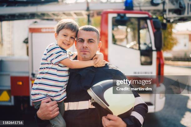 porträt des feuerwehrmannes hält kleinen jungen an den händen - father and children volunteering stock-fotos und bilder