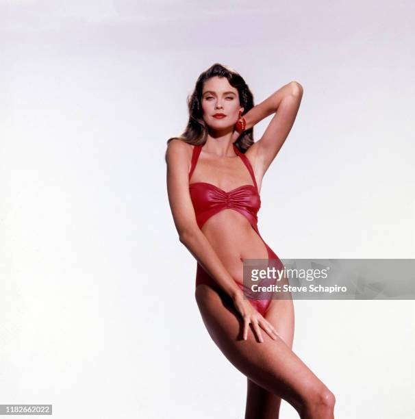 Portrait of American model and actress Carol Alt, in a red, one-piece swimsuit, as she poses against a white background, Los Angeles, California,...