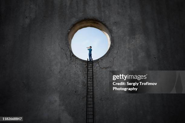 light hole in dark wall and man stands on a step ladder - catalejo fotografías e imágenes de stock