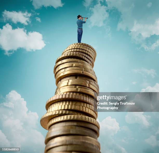 man standing on stack of coins and looking at telescope - coin stack stock-fotos und bilder