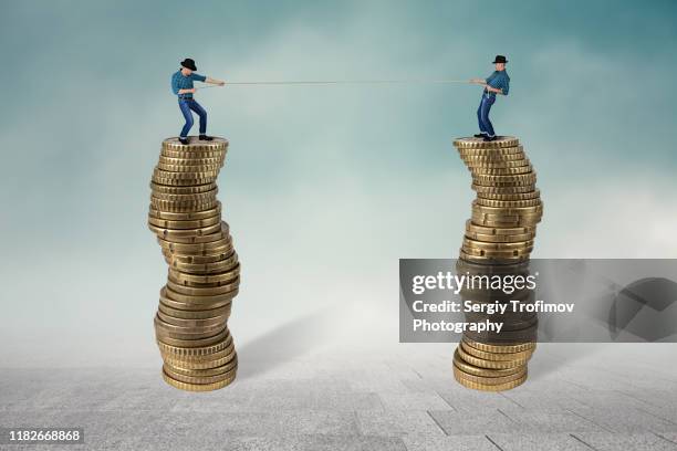 two men on top of coins in tug of war, business competition concept - equal pay stock-fotos und bilder