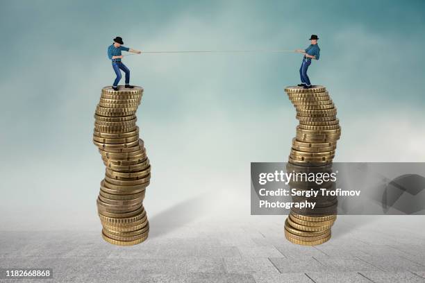 two men on top of coins in tug of war, business competition concept - salary stock pictures, royalty-free photos & images