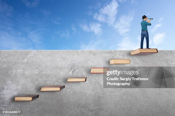 man on top of wall with books like stairs. looking at telescope - climbing ladder of success stock pictures, royalty-free photos & images