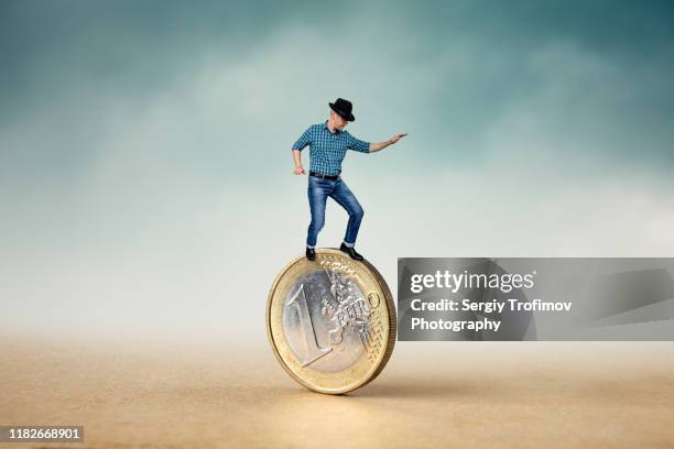 man riding a coin and balancing on top, financial concept - moeda de um euro imagens e fotografias de stock