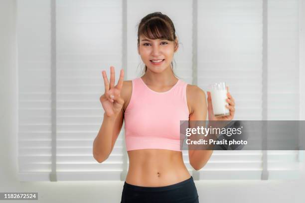 asian woman wearing pink sportswear drinking milk and happy and smiling beautiful young woman enjoying a glass milk and showing three fingers at home. people, food, beauty, lifestyle concept. - 3 fingers stockfoto's en -beelden