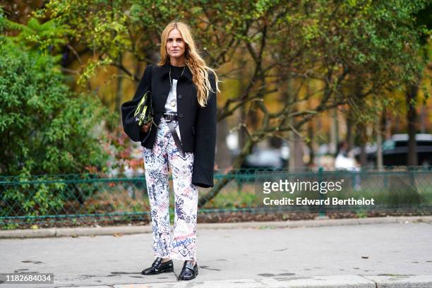 Blanca Miro wears a black oversized jacket, a leather belt, pants with printed graffiti, black leather shoes, a bag, outside Margiela, during Paris...