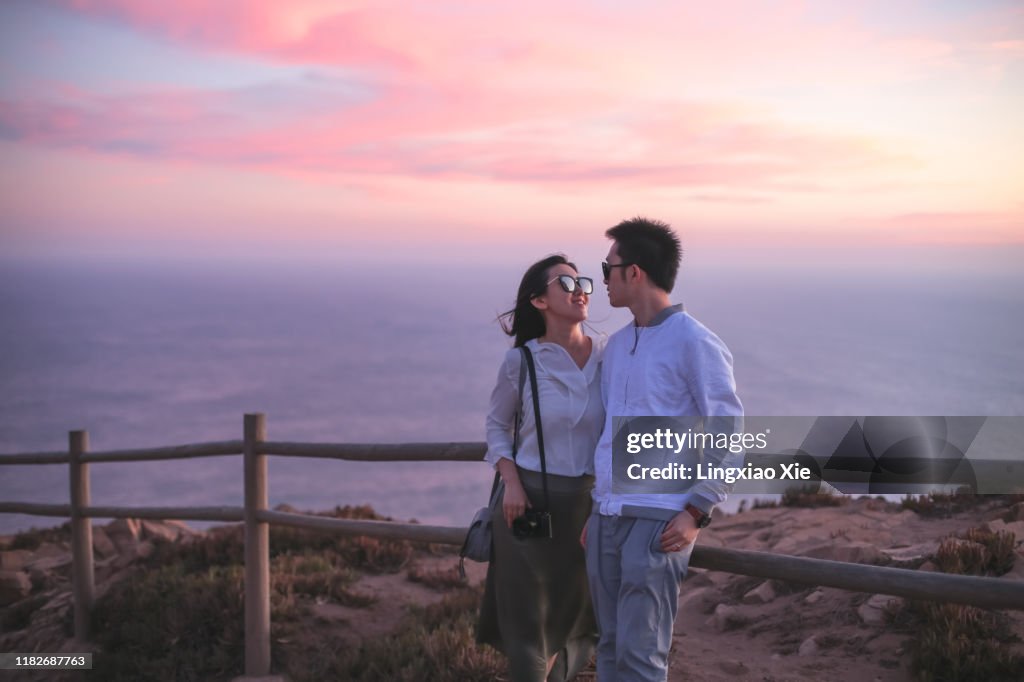 Couple standing along Atlantic coastline of Cape Roca at sunset, Sintra, Portugal