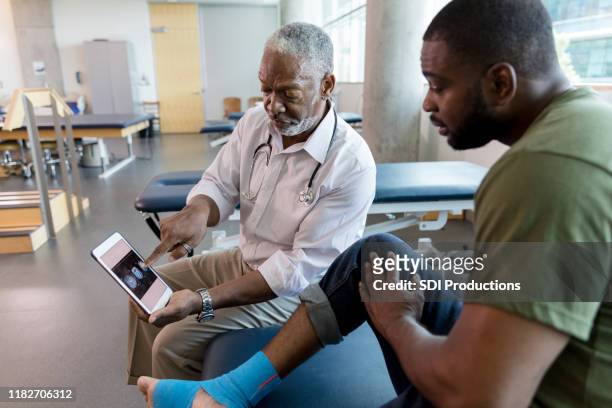 médico adulto maduro explica radiografías en tableta a paciente - black male feet fotografías e imágenes de stock