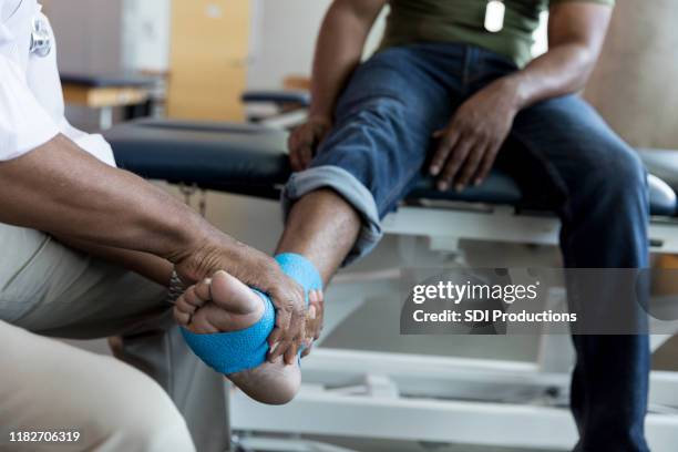 médico masculino irreconocible sostiene el pie herido de un veterano irreconocible - black male feet fotografías e imágenes de stock