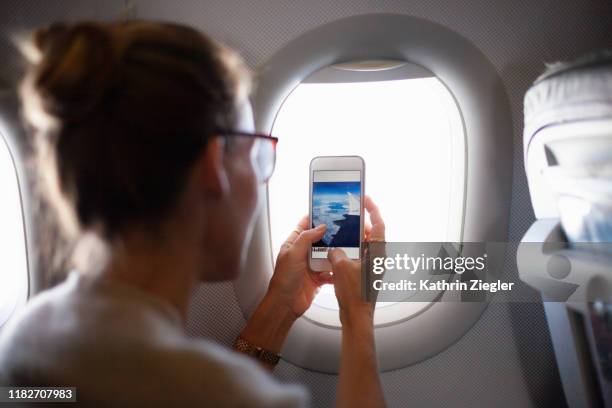 woman taking a photo through airplane window - airplane phone stock pictures, royalty-free photos & images