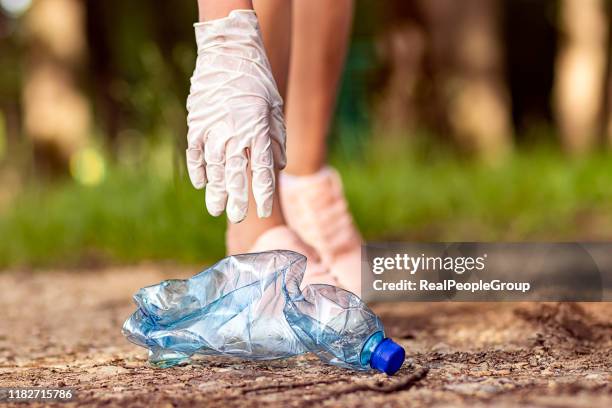 frau ehrenamtlich tragen abholung von müll und plastikmüll in öffentlichen park. junges mädchen trägt handschuhe und steckt wurf in schwarze plastiktüte im freien. - pick rubbish stock-fotos und bilder