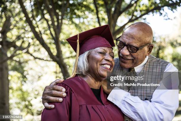 senior woman in college graduation gown with husband - graduation gown stock pictures, royalty-free photos & images