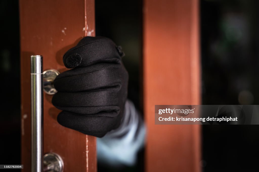 Dangerous masked burglar with crowbar breaking into a victim's home door,Home insurance concept