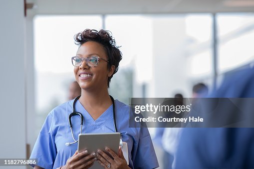 Female nurse or doctor smiles while staring out window in hospital hallway and holding digital tablet with electronic patient file Female nurse or doctor smiles while staring out window in hospital hallway and holding digital tablet with electronic patient file