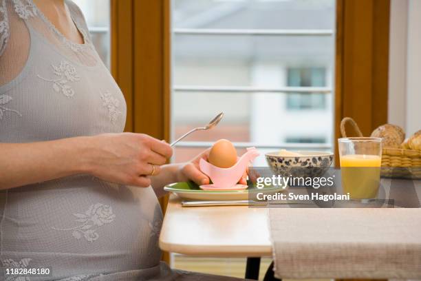 pregnant woman cracking a boiled egg at breakfast - crack spoon stock pictures, royalty-free photos & images