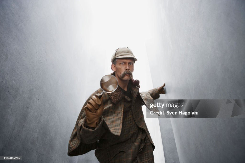 A man dressed like Sherlock Holmes holding a magnifying glass
