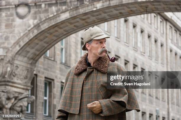 a man dressed up as sherlock holmes standing under a building arch looking away - sherlock imagens e fotografias de stock