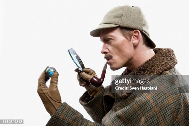 a man dressed up as sherlock holmes looking at a tiny globe through a magnifying glass - sherlock holmes imagens e fotografias de stock