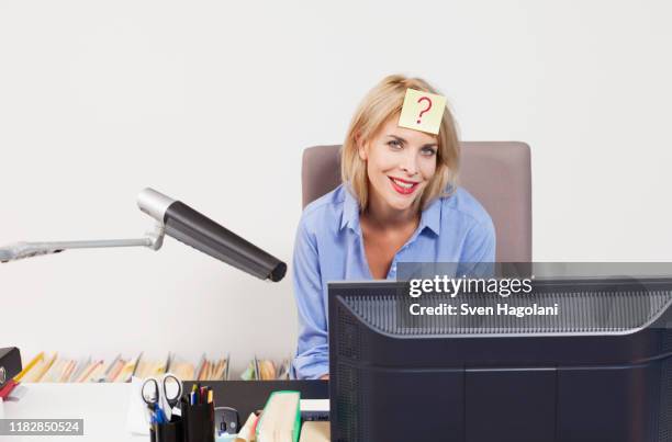 a woman sitting at an office desk with an adhesive note on her forehead - sticky notes covering computer monitor stock-fotos und bilder