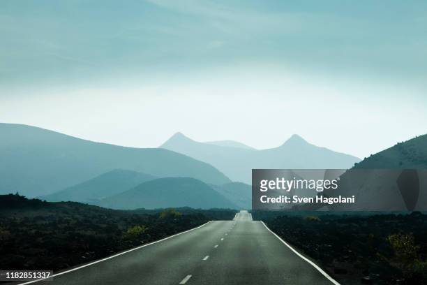 empty road leading towards mountains in lanzarote, canary islands, spain - horizonte sobre tierra fotografías e imágenes de stock