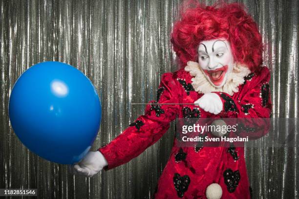 a clown getting ready to pop a balloon with a needle - clown photos et images de collection