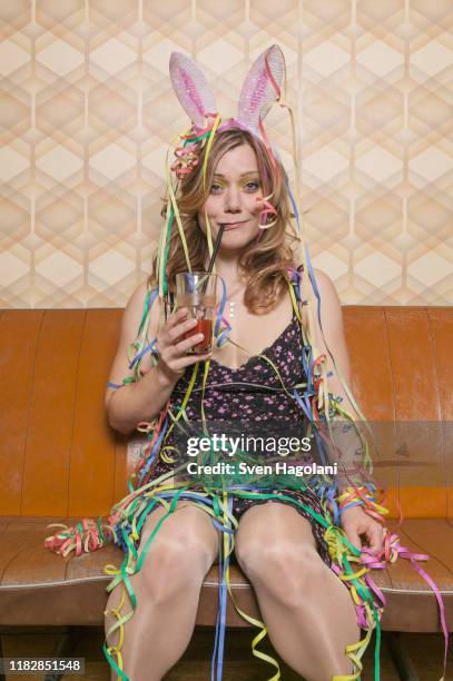 a tipsy woman drinking a cocktail and covered in streamers, portrait - drunk stockfoto's en -beelden