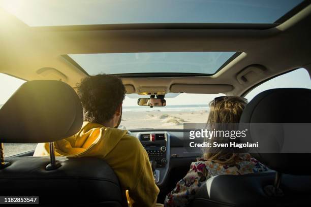 rear view of couple in car at beach on sunny day - car sunroof stockfoto's en -beelden