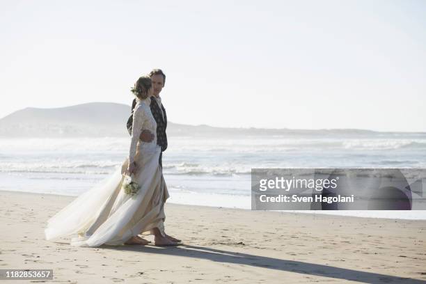 full length of loving bride and groom walking at beach - bride walking stock pictures, royalty-free photos & images