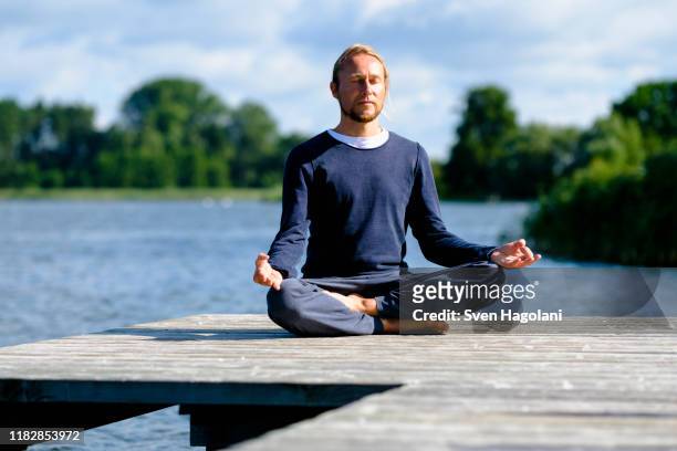 mature man practicing lotus position on pier by lake against sky - 胡坐　横 ストックフォトと画像