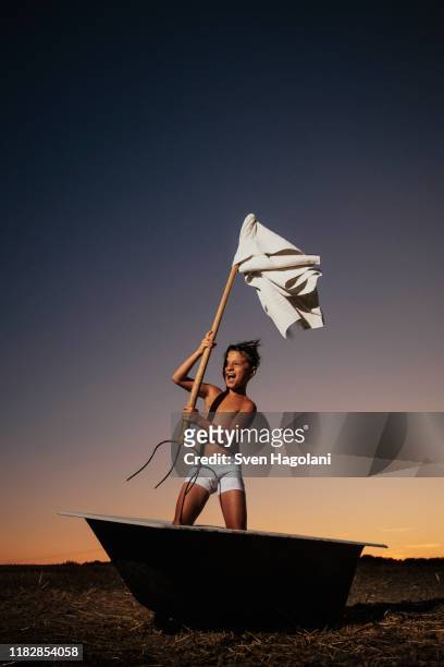 playful boy in underwear waving pitchfork white flag in bathtub in rural field - surrendering stock-fotos und bilder
