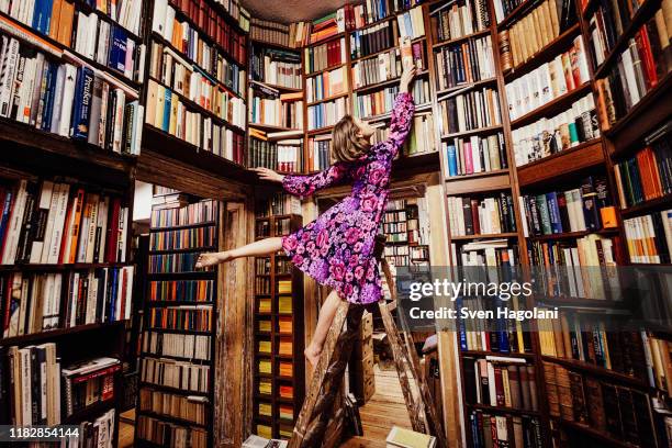 carefree woman on ladder reaching for book in library - floral pattern dress stock-fotos und bilder