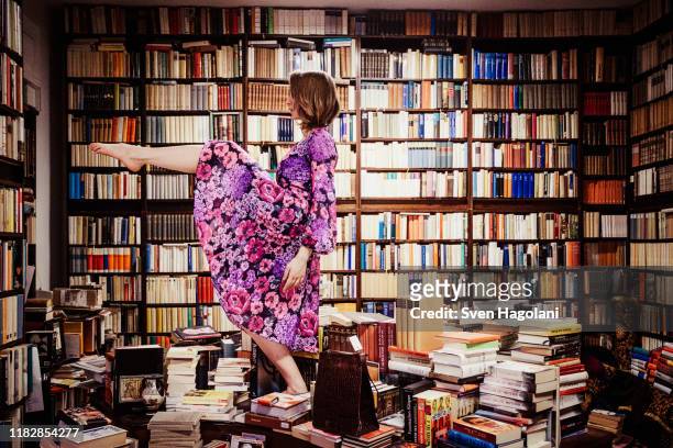 exuberant woman dancing on book stacks in library - floral pattern dress stockfoto's en -beelden