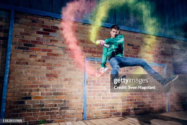 portrait male modern dancer performing with spray paint against brick wall - sprayer graffiti stock-fotos und bilder