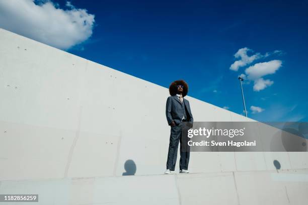 portrait confident, cool, well-dressed young man with afro standing on urban wall - geschäftskleidung stock-fotos und bilder