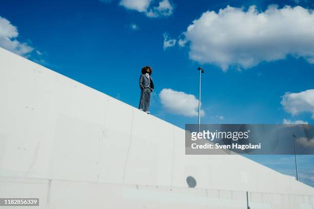 cool, well-dressed young man with afro standing on sunny urban wall - determination stock-fotos und bilder