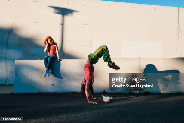 young woman watching man do handstand along urban wall - leben in der stadt stock-fotos und bilder