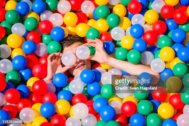 playful young man laying in multicolor ball pool - bedecken stock-fotos und bilder