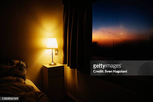 bedside lamp illuminating bedroom corner next to window with view of dusk sky - bedroom window foto e immagini stock