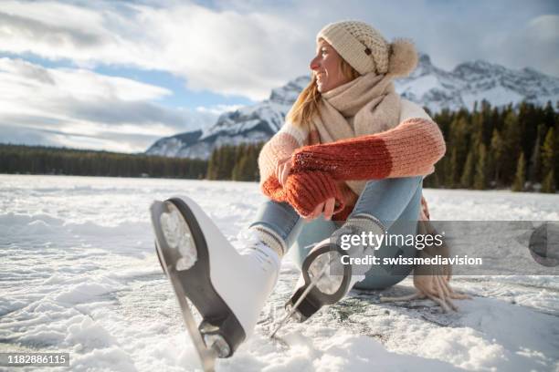 young woman on frozen lake putting on ice skates at sunset getting ready to have fun and enjoy winter vacations - ice skate stock pictures, royalty-free photos & images