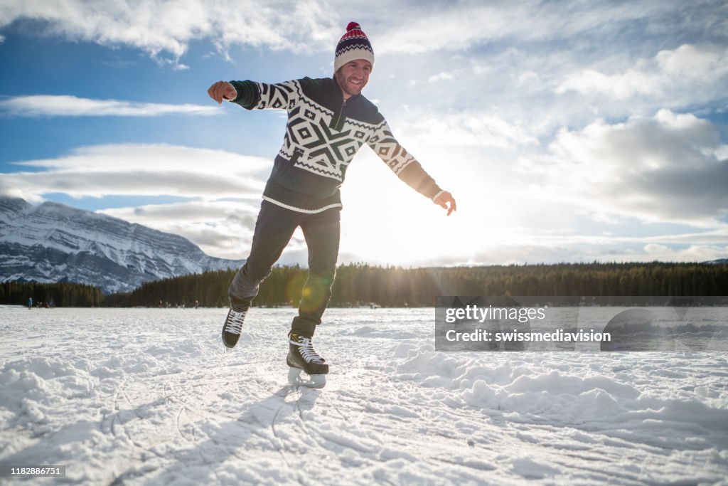 Young man ice skating on frozen lake at sunset having fun and enjoying winter vacations
