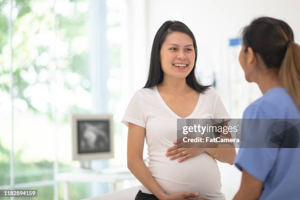 hispanic pregnant woman speaks with her doctor at a check-up stock photo - pregnancy appointment stock pictures, royalty-free photos & images