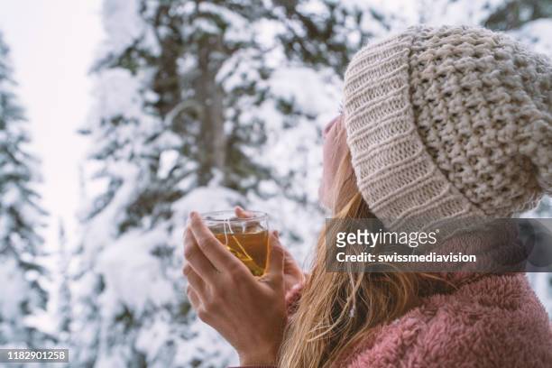 woman in log cain looking at the snow falling with tea cup in hands - pink hat stock pictures, royalty-free photos & images