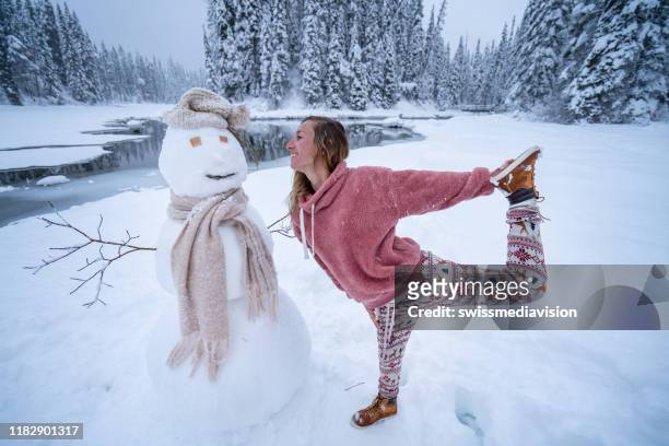 es ist weihnachtszeit - frau posiert mit schneemann im winterurlaub - yoga in the snow stock-fotos und bilder
