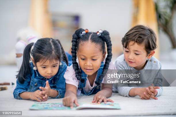 un groupe de trois enfants multi-ethniques se sont couchés sur le plancher lisant ensemble la photo de stock - 4 5 ans photos et images de collection