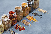 Assortments of spices, white pepper, chili flakes, lemongrass, coriander and cumin seeds in jars on grey stone background. Copy space.