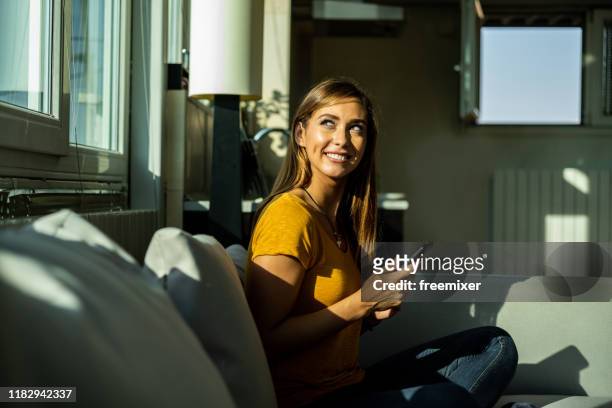 bella donna seduta sul divano in soggiorno - soleggiato foto e immagini stock