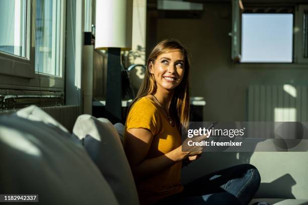 beautiful woman sitting on sofa in living room - rapariga no quarto tecnologia imagens e fotografias de stock