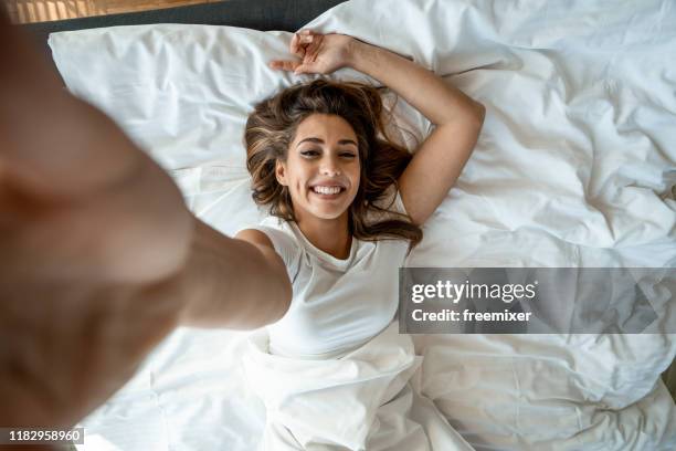 beautiful woman lying on bed and taking selfie - selfie bed stock pictures, royalty-free photos & images
