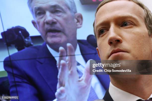 With an image of Federal Reserve Bank Chairman Jerome Powell on a screen in the background, Facebook co-founder and CEO Mark Zuckerberg testifies...